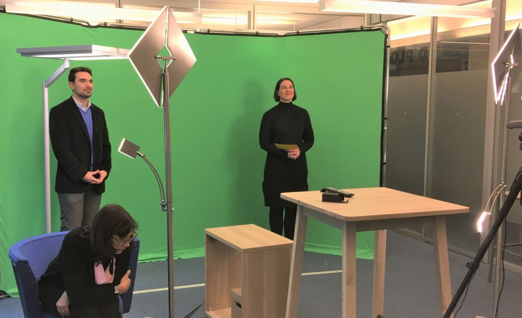 conftech-geneva-04 Furniture, Table, Desk, Adult, Male, Man, Person, Female, Woman, Crowd, Lamp, Audience, Standing Desk, Clothing, Coat, Face, Head, Electronics, Remote Control, Speech