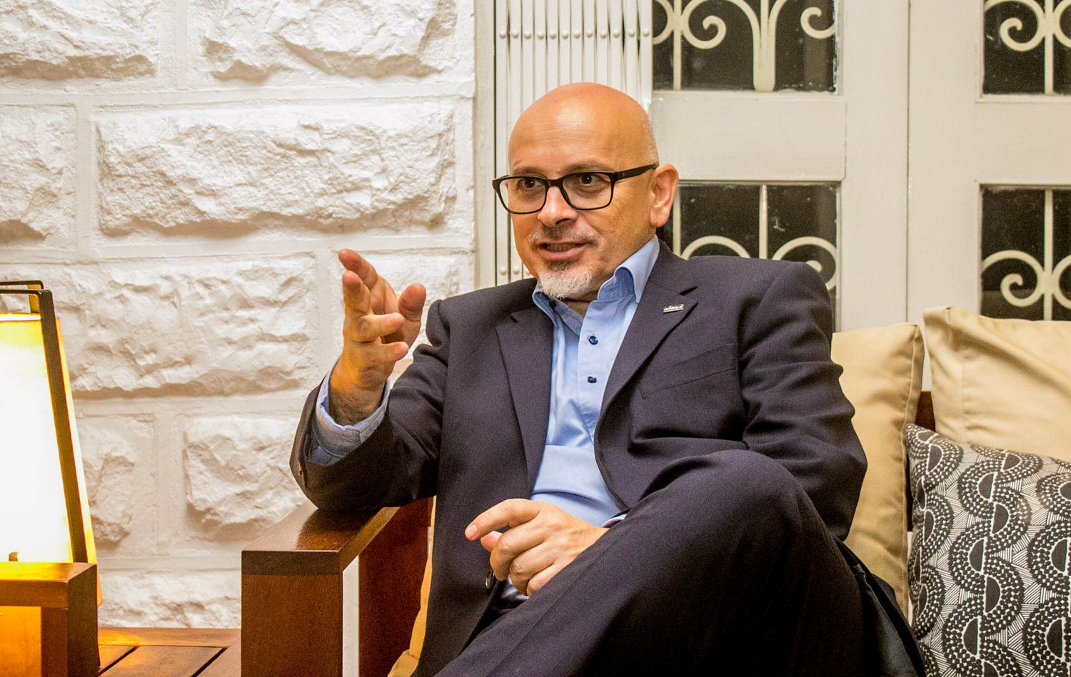  Clothing, Formal Wear, Suit, Adult, Male, Man, Person, Sitting, Lamp, Face, Head, Body Part, Finger, Hand, Accessories, Glasses