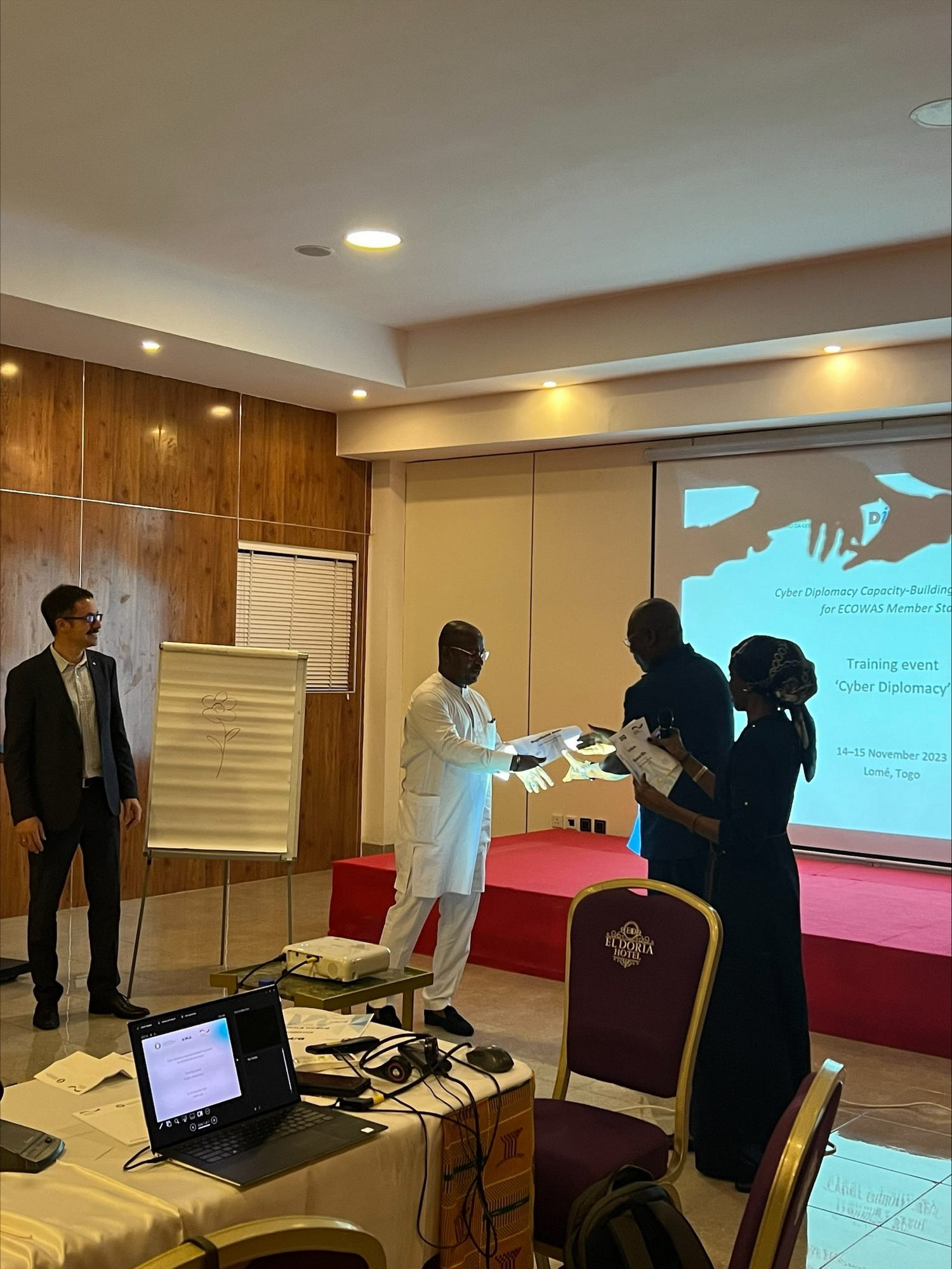  Crowd, Person, Adult, Male, Man, Clothing, Glove, Computer, Electronics, Laptop, Pc, Audience, Footwear, Shoe, Accessories, Glasses, Speech, Computer Hardware, Hardware, Monitor, Screen, Chair, Furniture, Coat