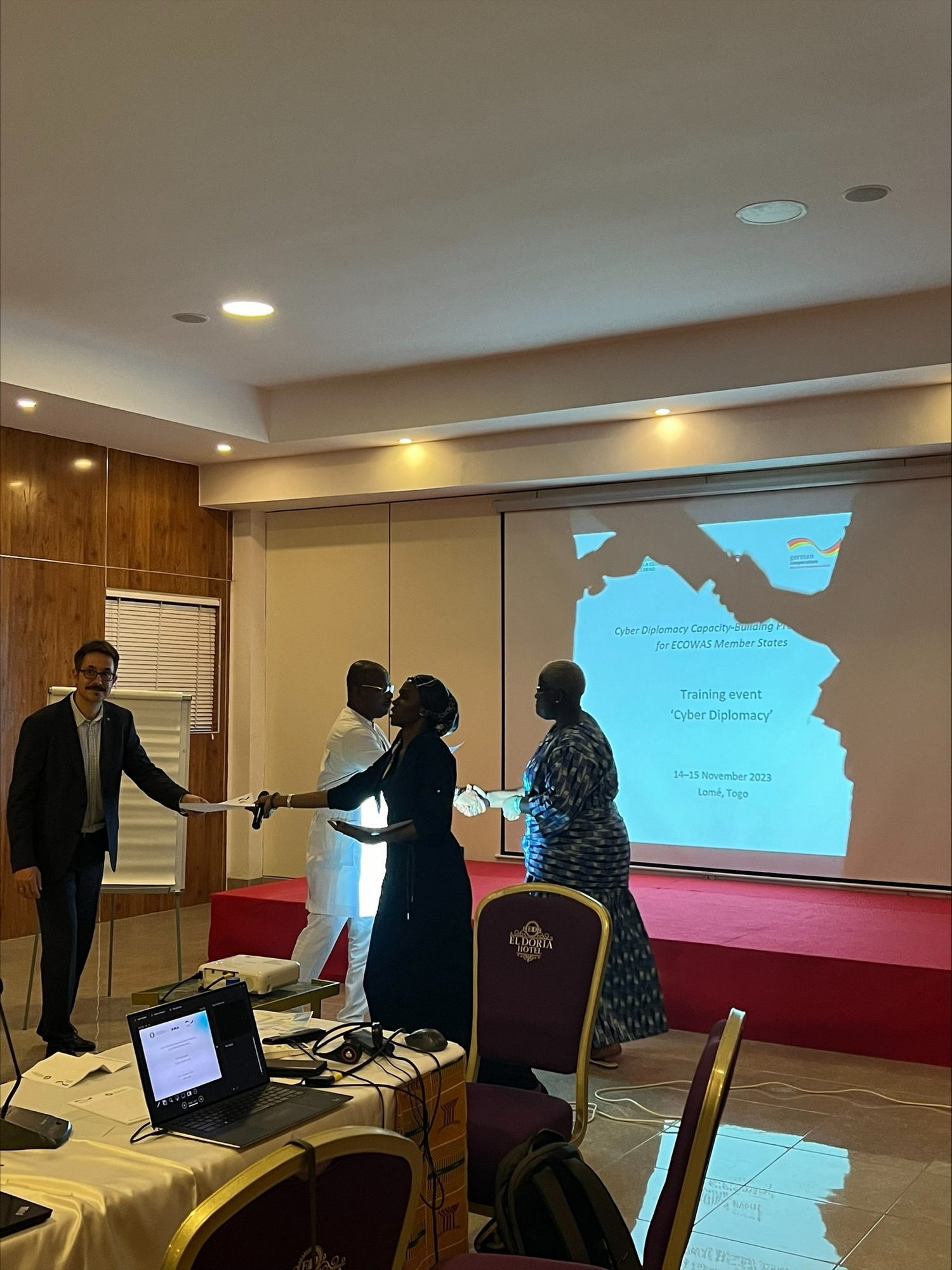  Crowd, Person, Adult, Male, Man, Audience, Computer, Electronics, Laptop, Pc, Accessories, Glasses, Indoors, Speech, Chair, Furniture, Clothing, Glove, Computer Hardware, Hardware, Monitor, Screen, Footwear, Shoe, Desk, Table, Sword, Weapon, Mouse