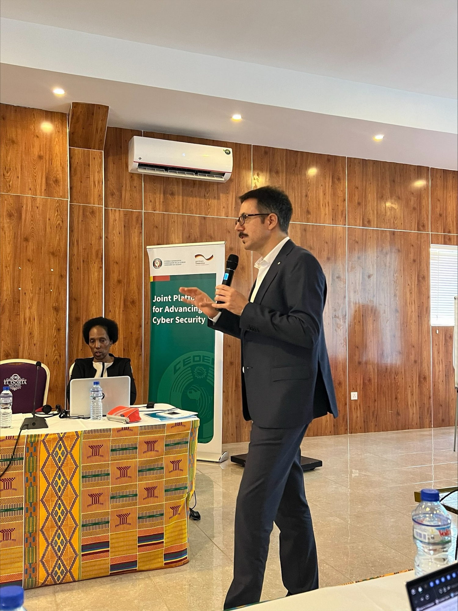  Crowd, Person, Audience, Adult, Female, Woman, Speech, Male, Man, Computer, Electronics, Laptop, Pc, Chair, Furniture, Electrical Device, Microphone, Mobile Phone, Phone, Headphones, Accessories, Glasses, Face, Head, Clothing, Coat