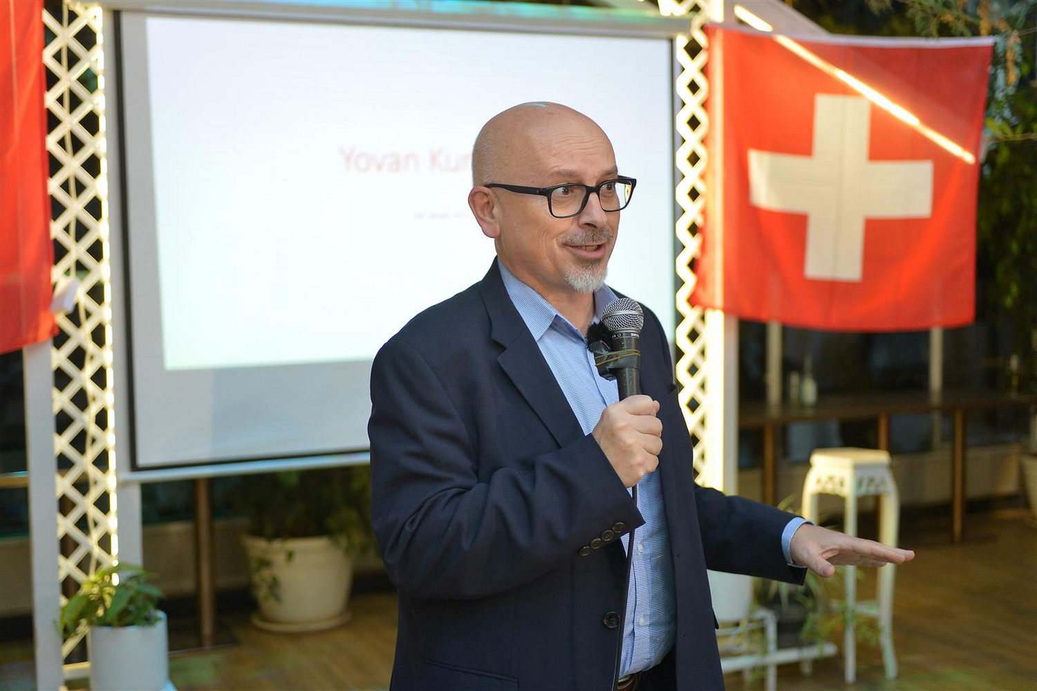  Flag, Adult, Male, Man, Person, Clothing, Formal Wear, Suit, Plant, Accessories, Glasses, Face, Head, Crowd, Switzerland Flag, Electrical Device, Microphone, Coat